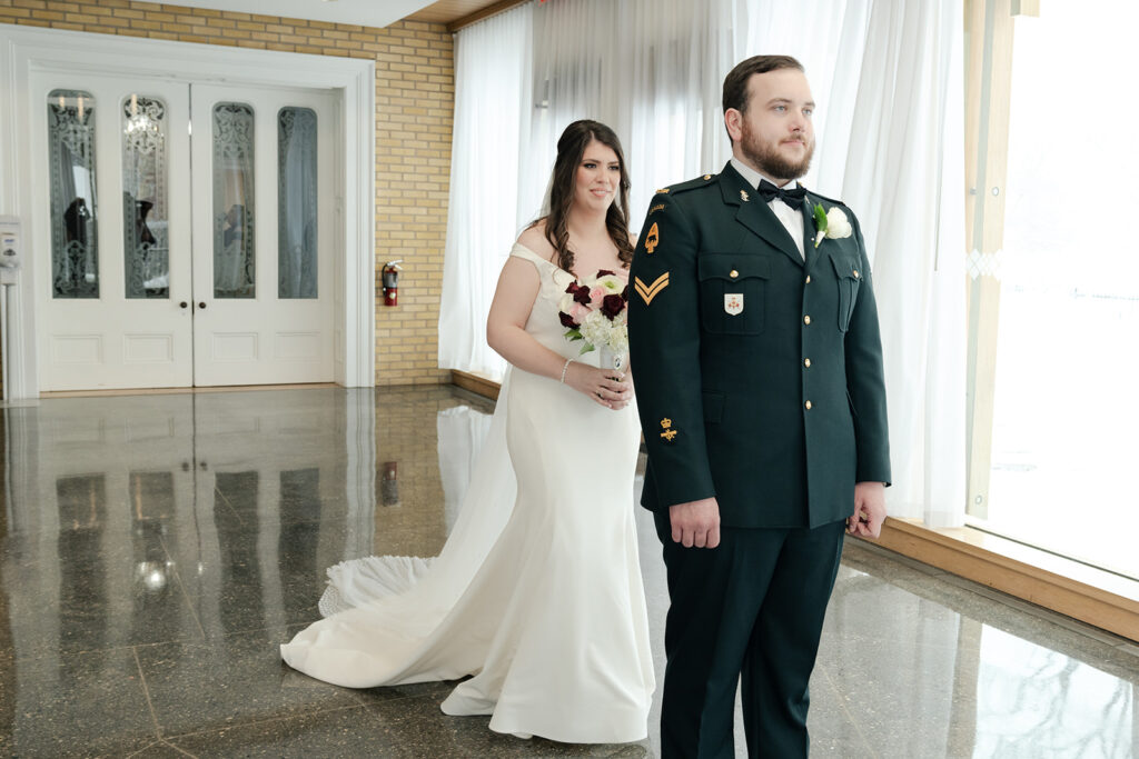 Bride and groom sharing a first look moment in a bright hallway, with the groom in military uniform and the bride smiling while holding a bouquet.