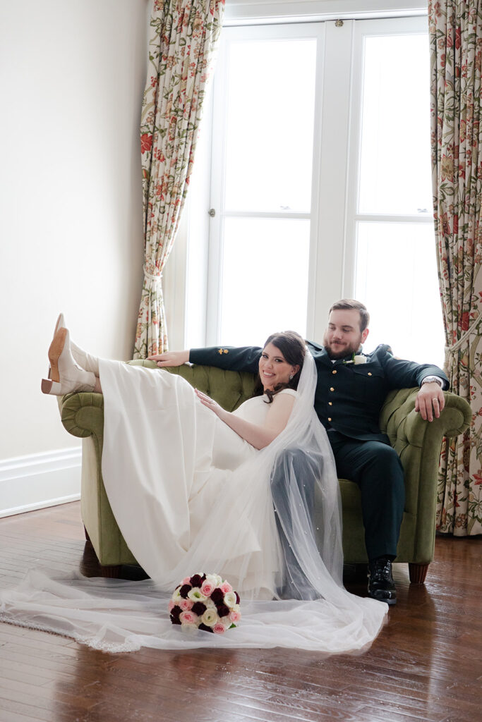 Bride and groom relaxing on a vintage couch, bride playfully kicking up her heels.