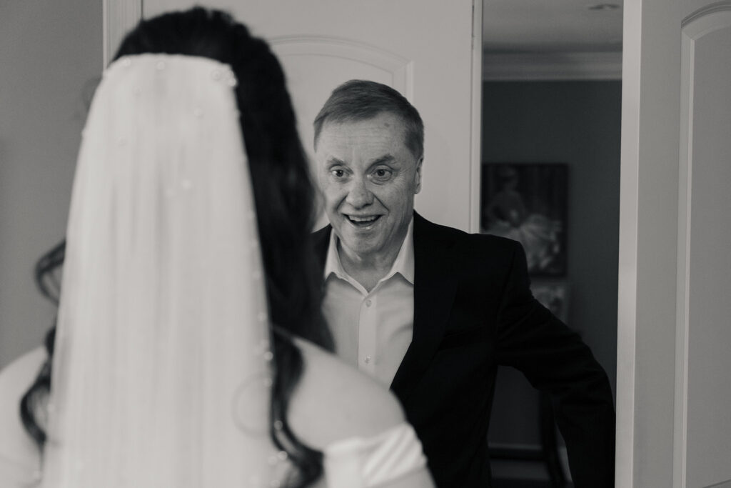 Father of the bride in a suit, looking lovingly at his daughter on her wedding day, captured in a timeless black and white photograph.