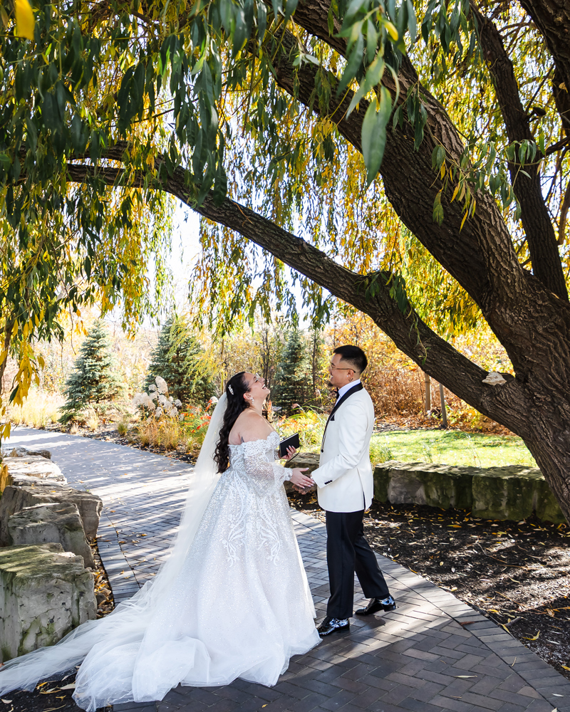 Bride and groom share a joyful first look moment under a tree on their wedding day