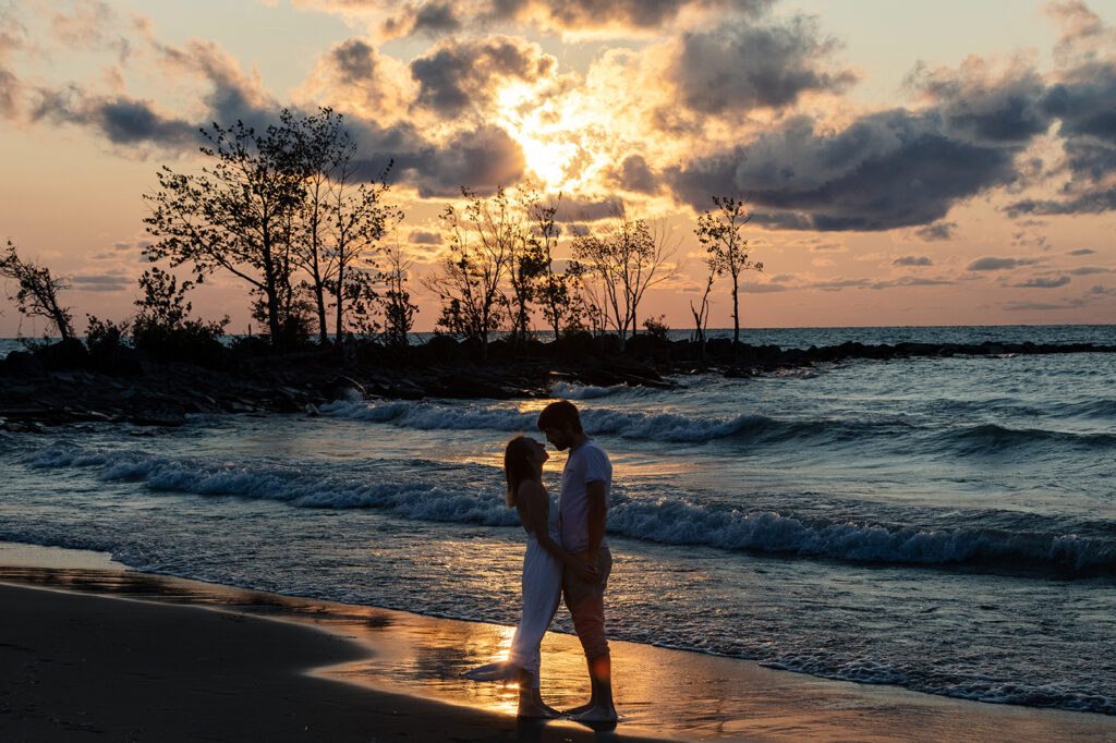 almost kiss on a beach during sunset with the wave crashing in the golden sun. The sky is dramatic with the cloud floating by and the pink sky and cyan blue water