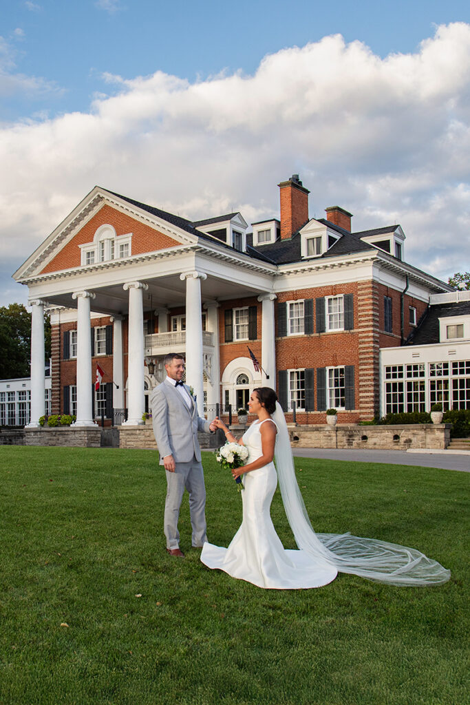 Bride and groom on the Langdon Hall lawn with columns behind—grand architecture wedding portrait, candid.