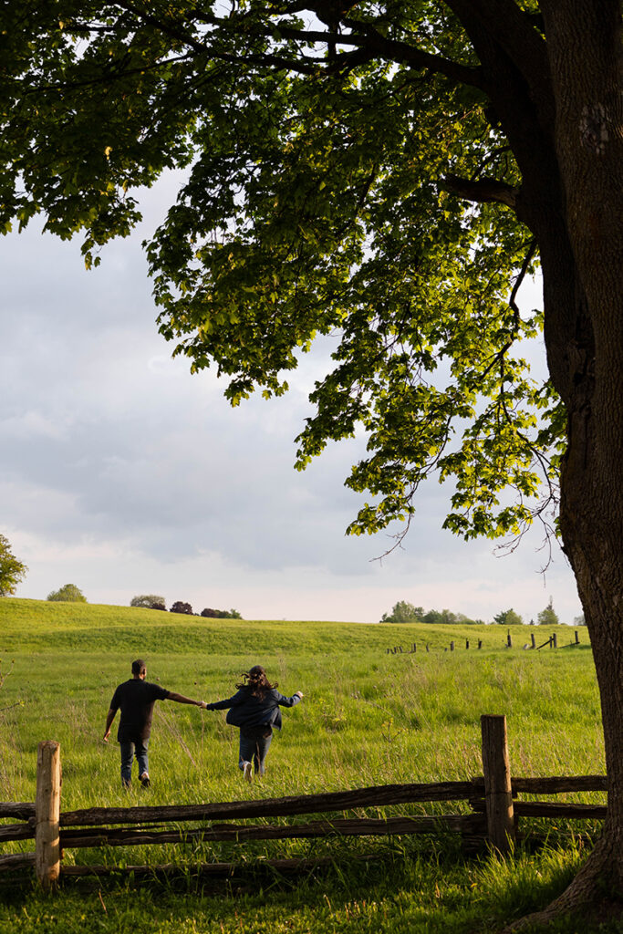 Couple running through a sunlit field at Scottsdale Farm—joyful, candid engagement photo.