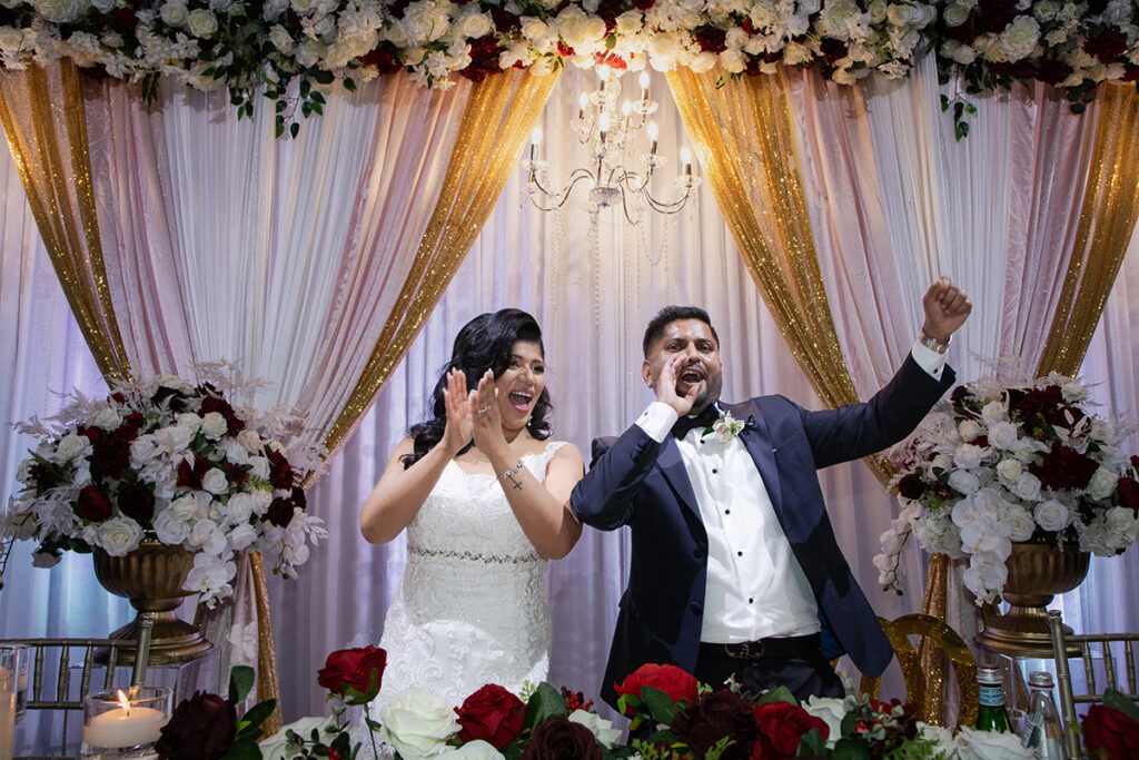 Bride and groom cheering at the head table during reception entrance—candid celebration photo